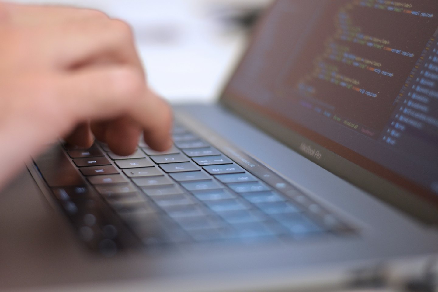 Hände tippen Programmiercode auf einer Laptop-Tastatur.